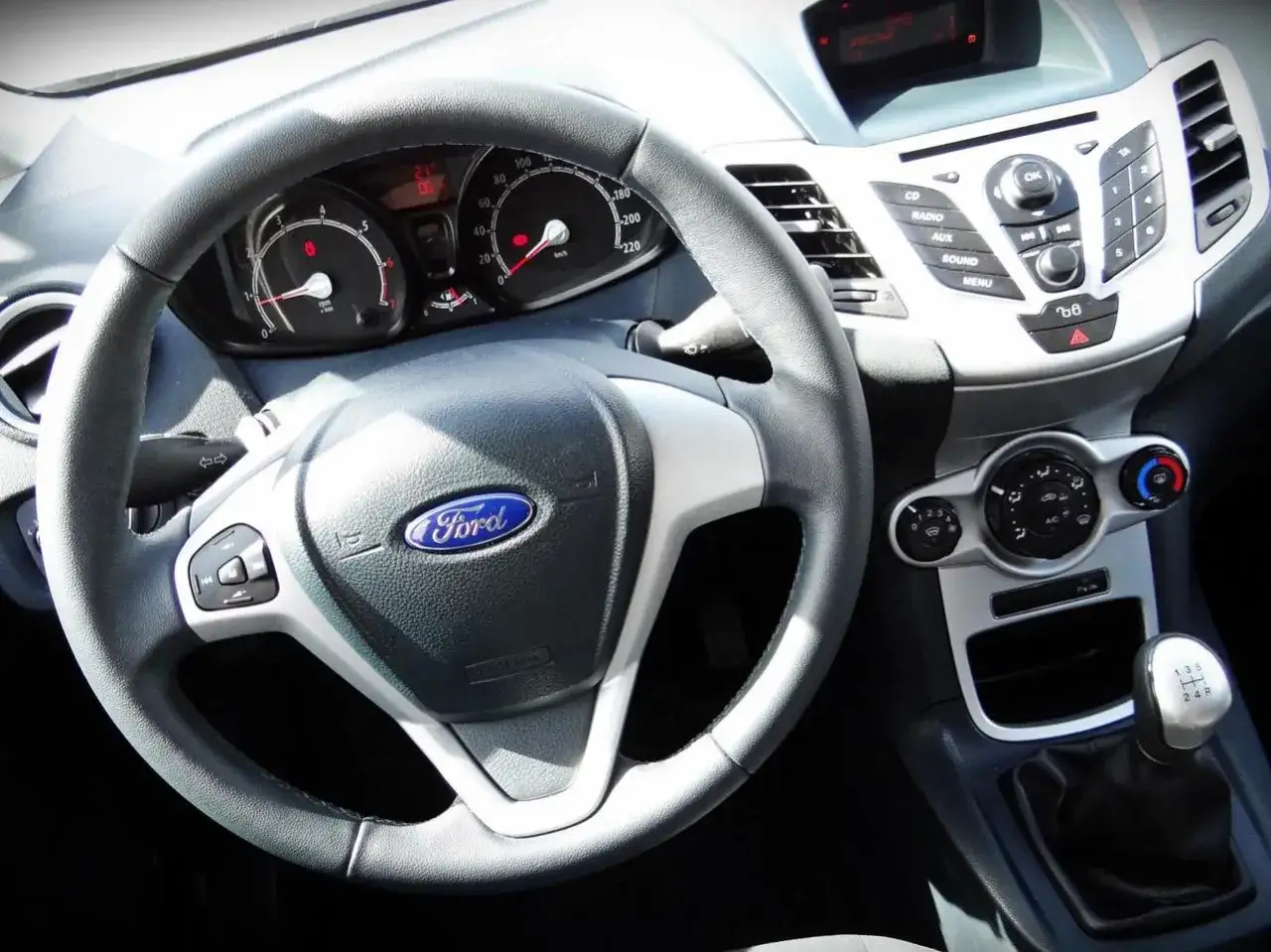 Wnętrze Ford Fiesta 2011: kierownica, deska rozdzielcza z radiem i nawiewami, dźwignia zmiany biegów.