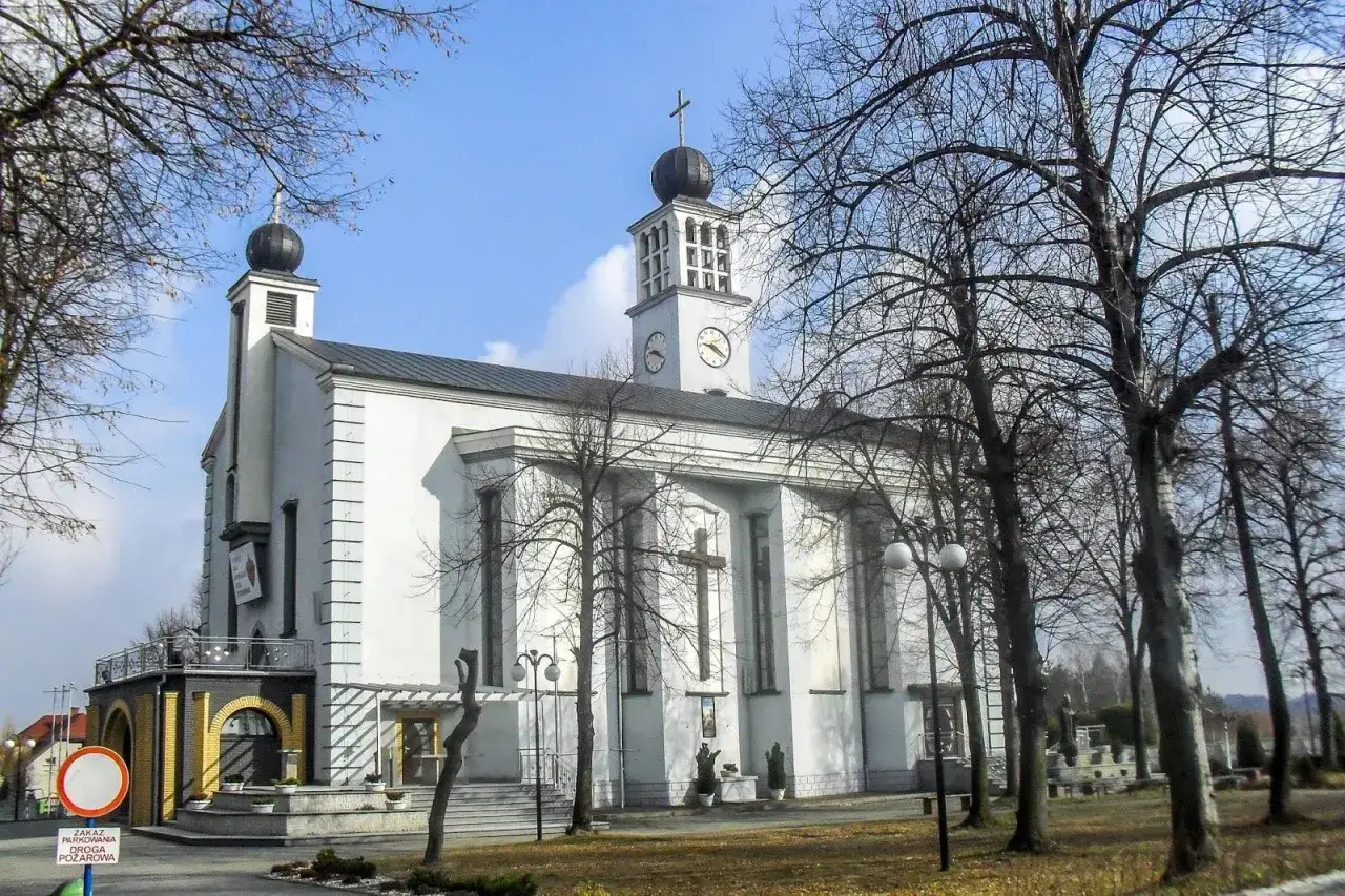 Biały kościół z wieżą zegarową i krzyżem na froncie, otoczony nagimi drzewami. To charakterystyczny widok turzy śląskiej.