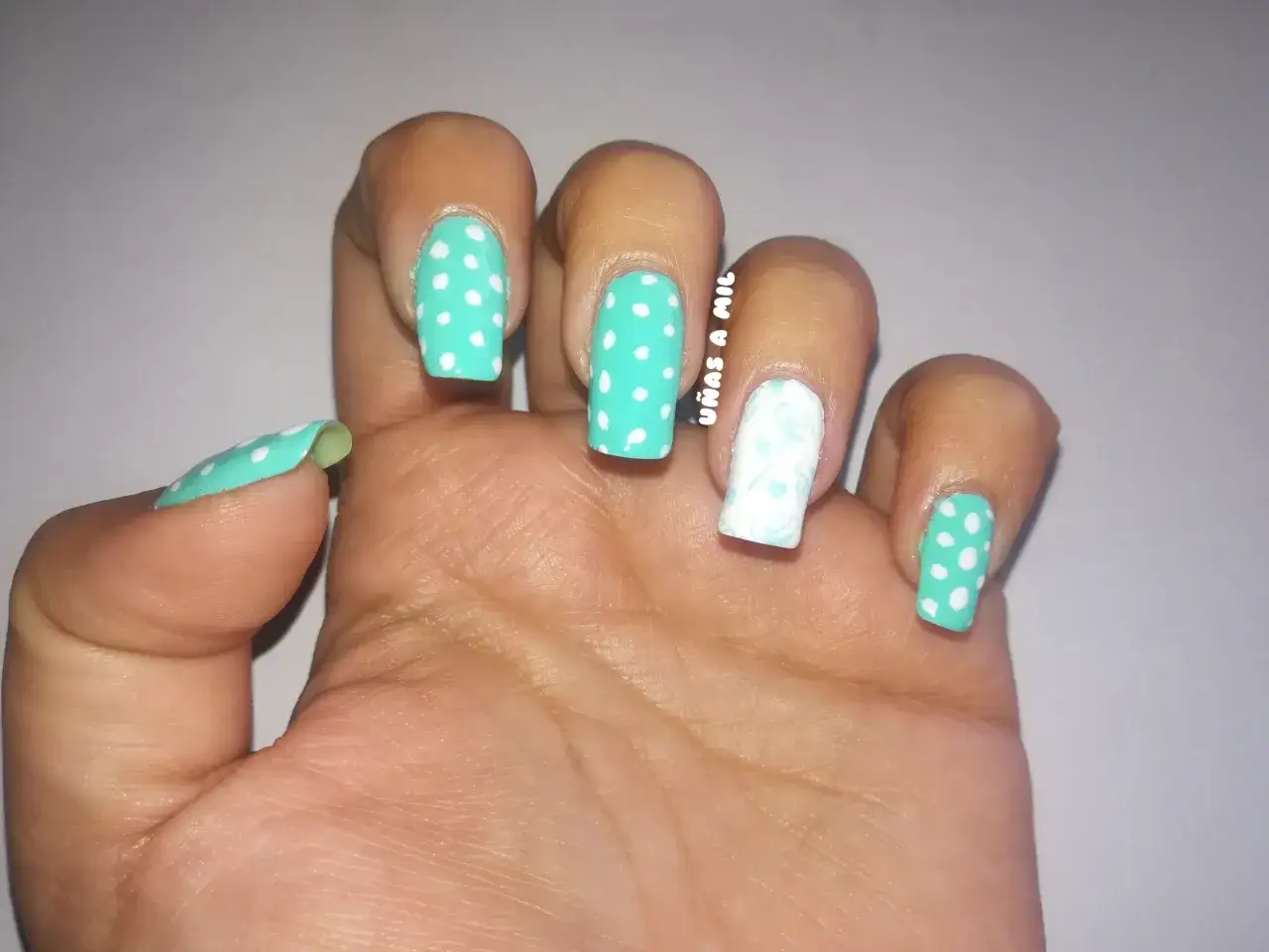 U&ntilde;as sevillanas con dise&ntilde;o de lunares blancos sobre fondo turquesa y un dedo decorado con un delicado estampado floral blanco.