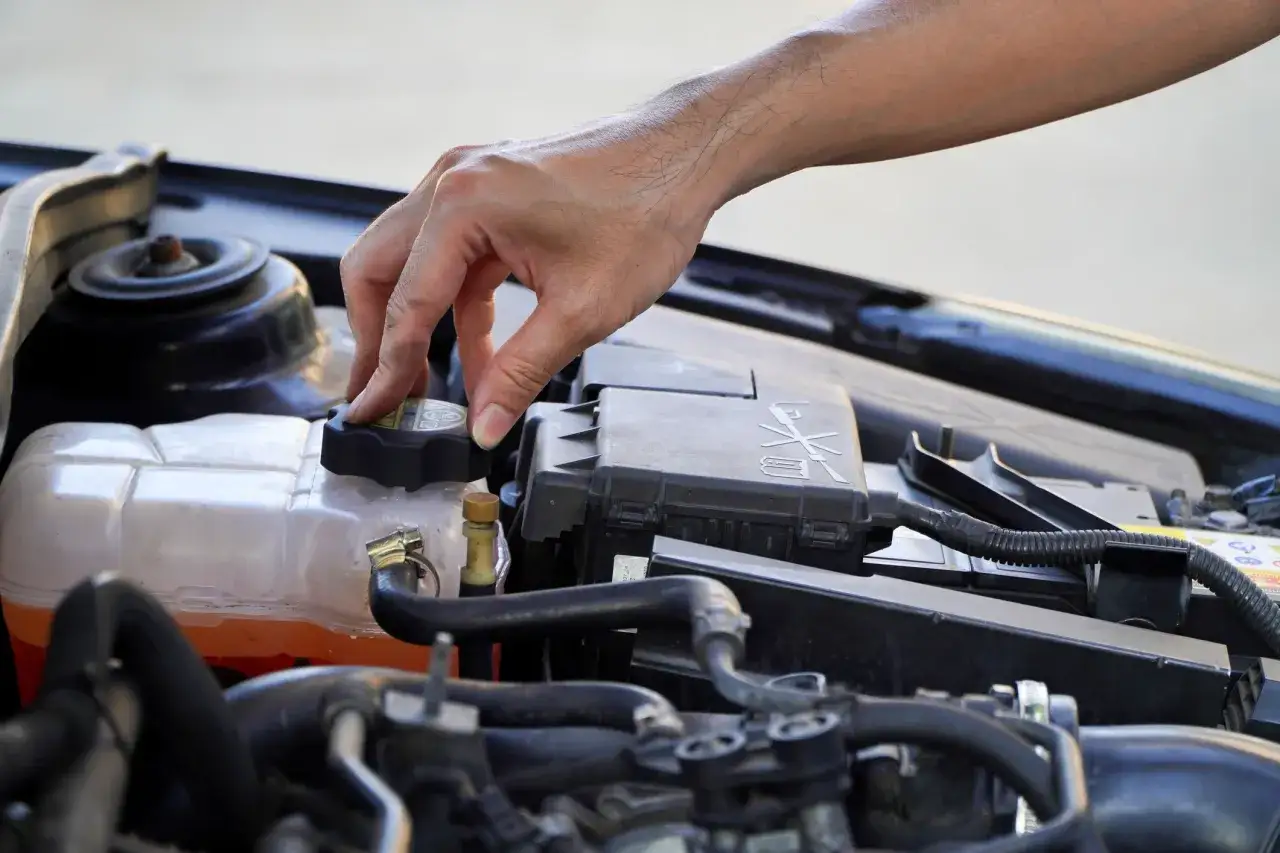 A hand twists the cap on a car's coolant reservoir, a step in learning how to dispose of antifreeze safely.