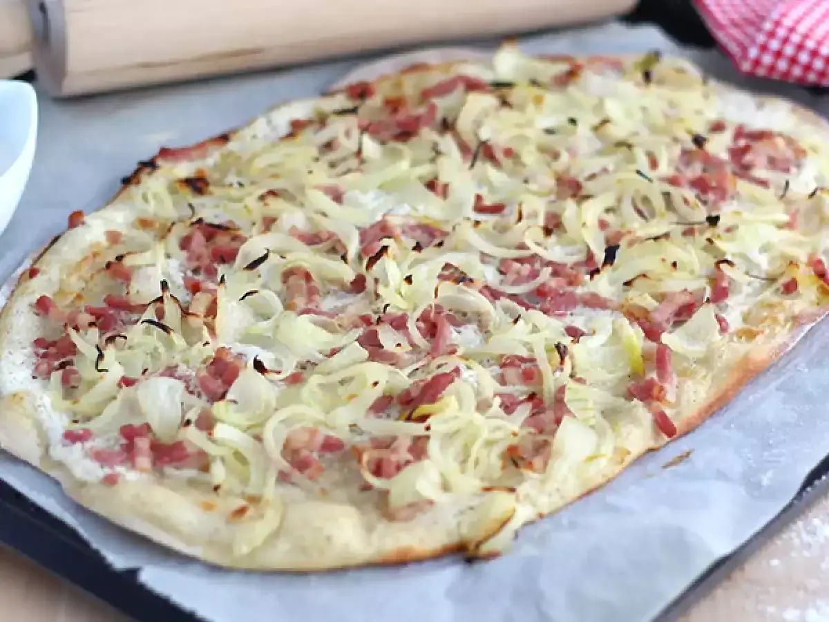 Une flammekueche dorée, garnie d'oignons et de lardons, prête à être dégustée.