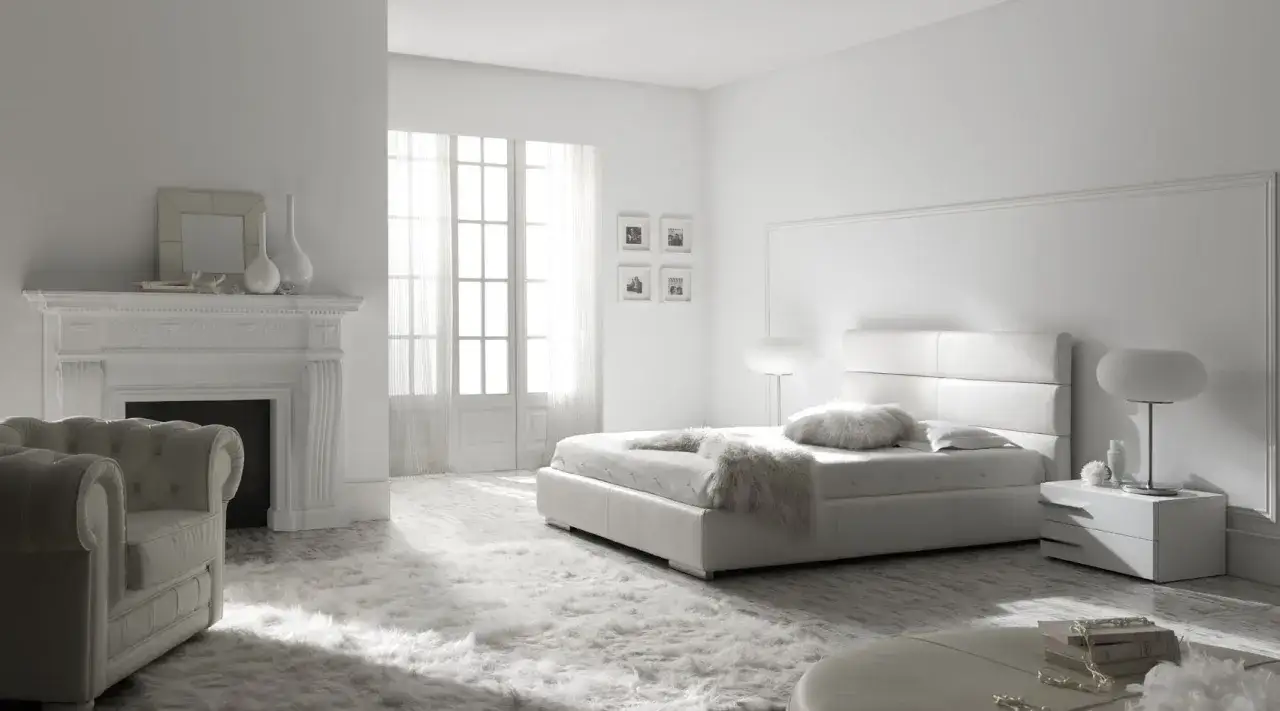 Dormitorio minimalista con cama blanca, chimenea y sillón, todo en **colores claros** que transmiten serenidad.