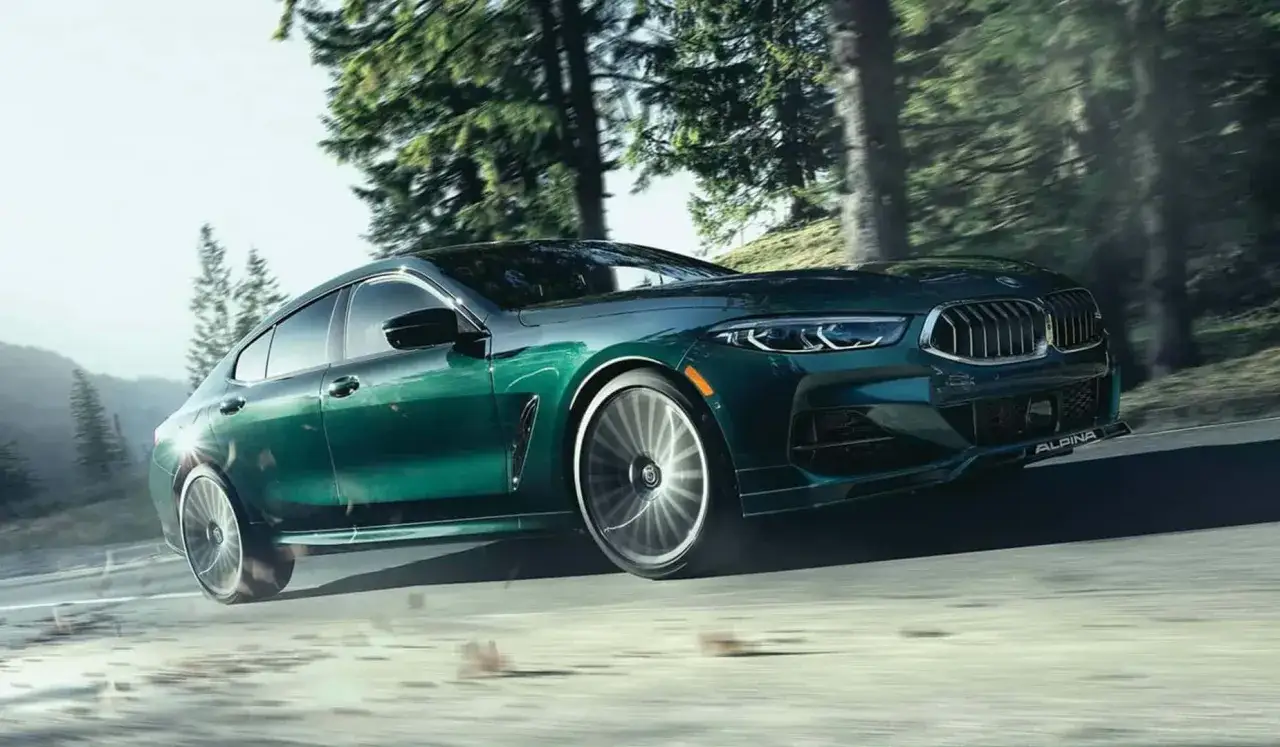 Zielony BMW Alpina pędzi leśną drogą, unosząc lekko koła.