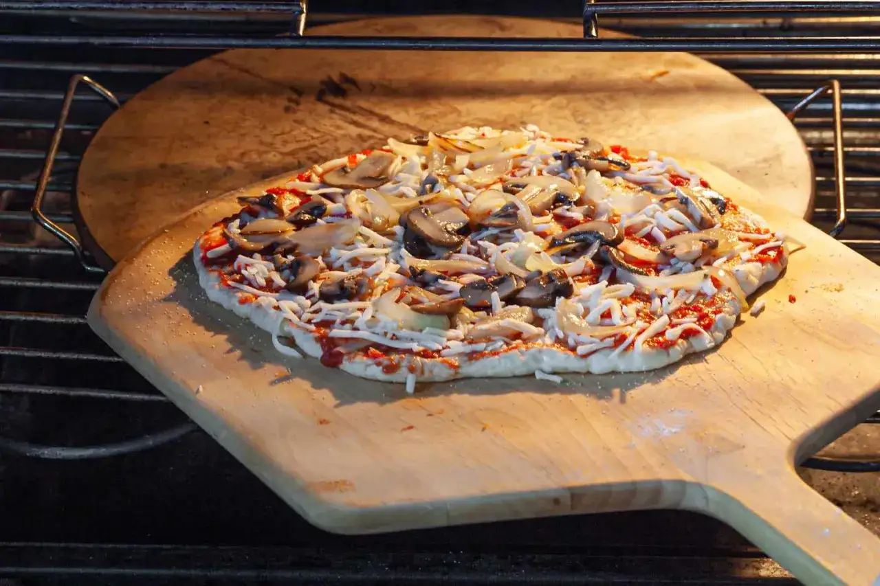 Eine rohe Pizza mit Pilzen und Zwiebeln wird auf einem Pizzastein im Ofen platziert. Ein perfektes italien pizza rezept für zu Hause.