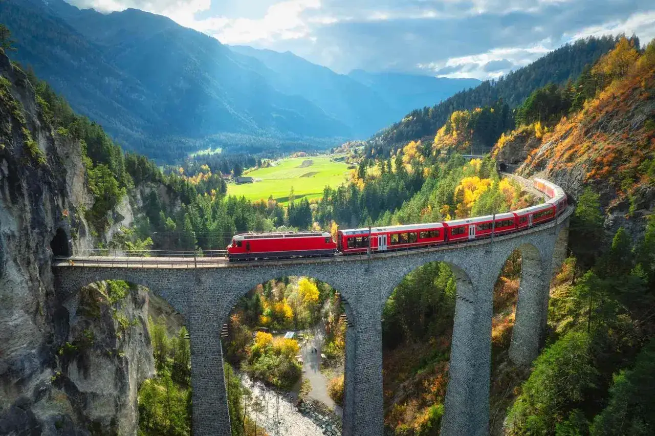 A red train travels across a stone viaduct in a lush valley, a scenic journey from Passau to Vienna.