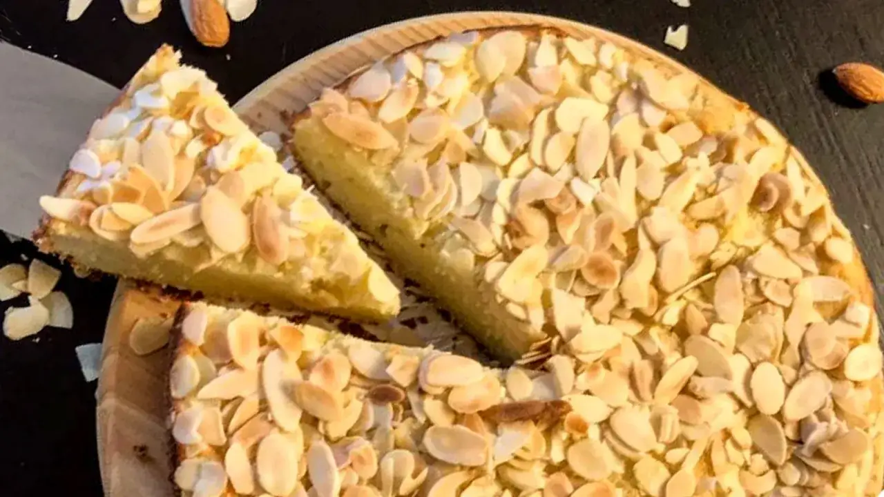 Torta con farina di mandorle, ricoperta di mandorle a lamelle tostate. Una fetta è stata tagliata e posizionata sopra.
