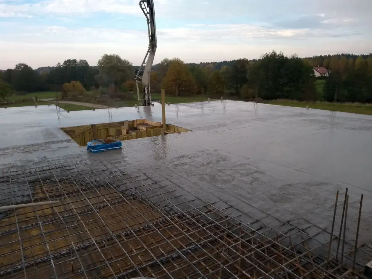 Pompa do betonu wylewa świeży beton na strop, tworząc solidną konstrukcję. Widać zbrojenie i szalunki.