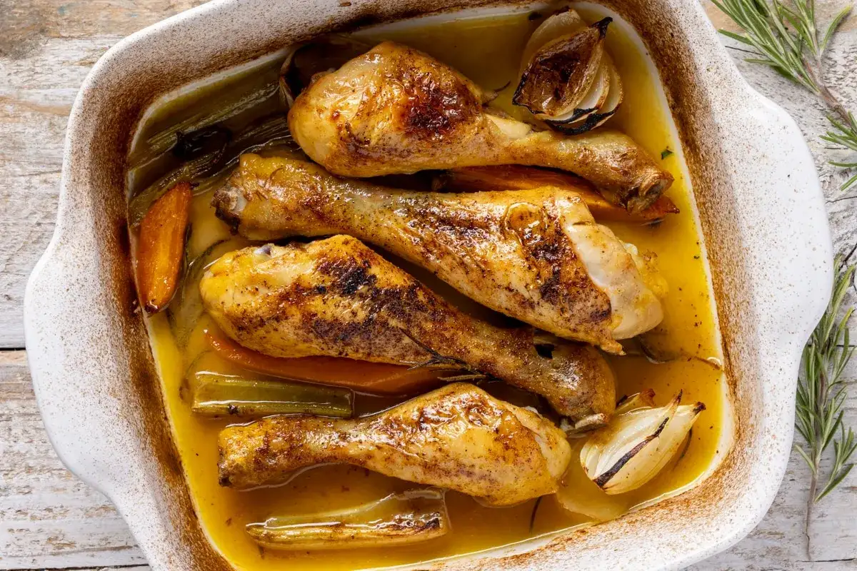Deliziosi fusi di pollo al forno, dorati e succulenti, cotti con verdure e aromi in una teglia bianca.