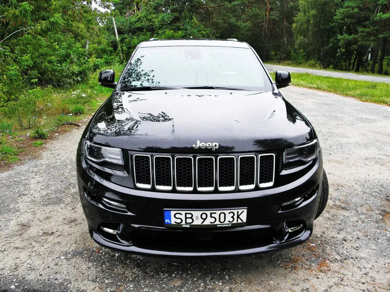 Czarny Jeep Grand Cherokee Trackhawk na leśnej drodze.
