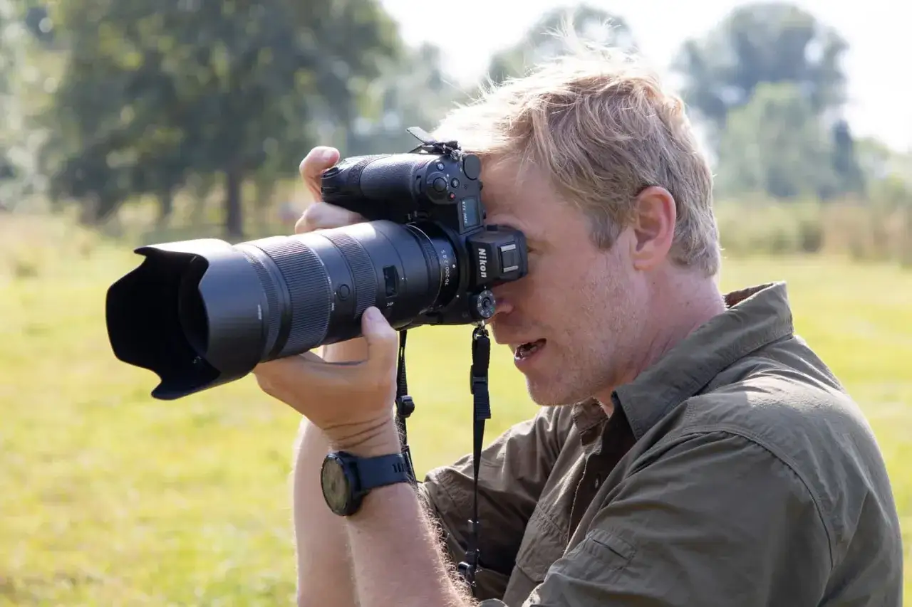 Mężczyzna z blond włosami testuje aparat Nikon Z7 II z długim obiektywem, skupiony na kadrze.