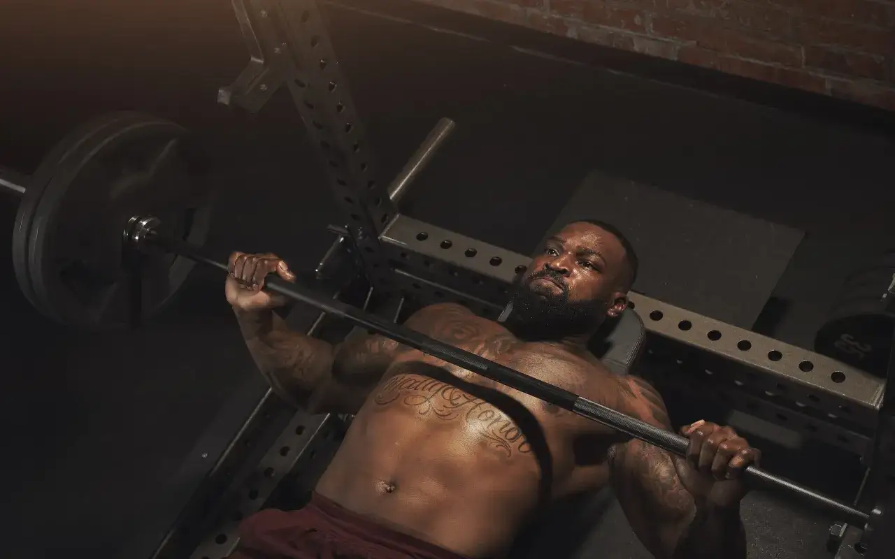 Mann mit Tattoos trainiert im Fitnessstudio, stemmt eine Langhantel. Er weiß, wie man richtig trainieren im fitnessstudio.