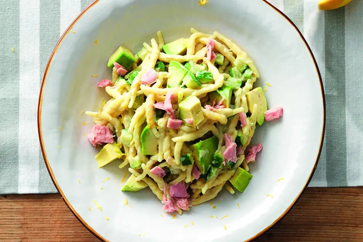 Pyszna pasta z awokado i tuńczyka, posypana skórką cytrynową, podana na białym talerzu.