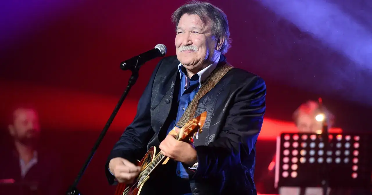 Andrzej Rybiński, mimo swojego wieku, wciąż z pasją gra na gitarze i śpiewa na scenie, otoczony scenicznym światłem.