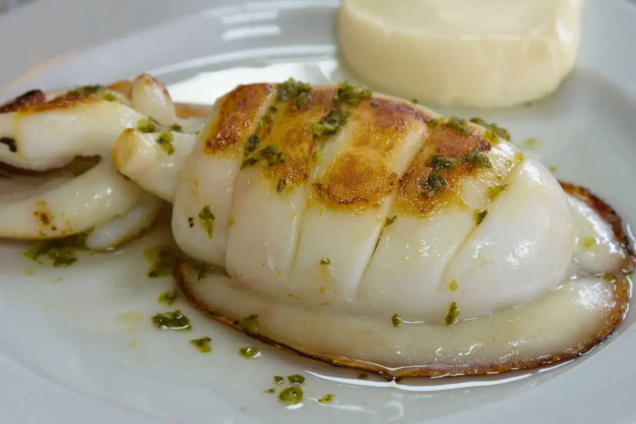 Sepia a la plancha con trocitos verdes y una porción de puré cremoso.