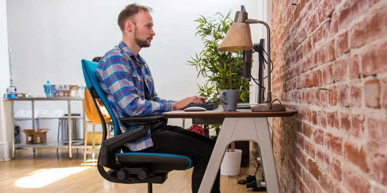 Homme travaillant &agrave; son bureau, adoptant une posture ergonomique. Son fauteuil bleu soutient son dos, favorisant un bon alignement.
