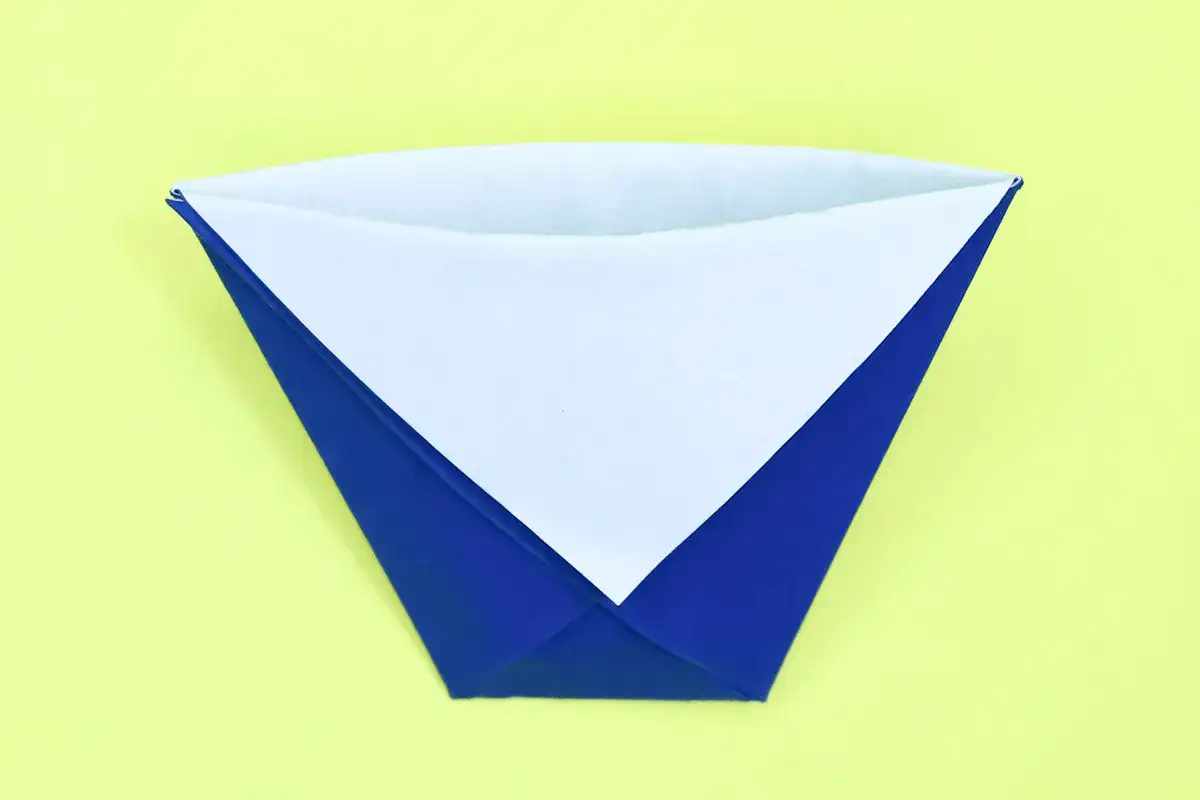 Ein gefalteter Papierbecher in Blau und Weiß auf gelbem Hintergrund. So einfach kann man einen Becher falten!