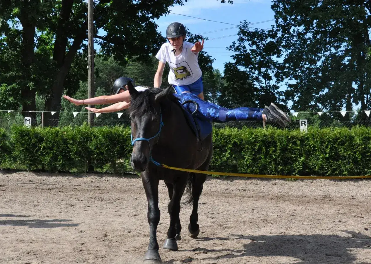 Dwie dziewczyny ćwiczą akrobacje na koniu w końskim gaju Tanowo. Jedna siedzi, druga stoi na grzbiecie.