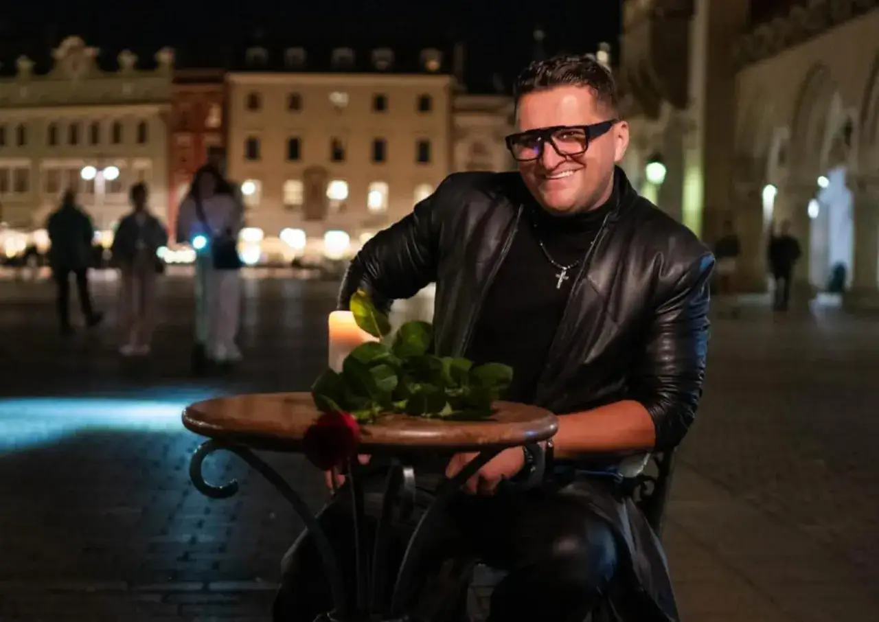 Uśmiechnięty mężczyzna w skórzanej kurtce siedzi przy stoliku z różą i świecą. Czy to Kordian Cieślik?