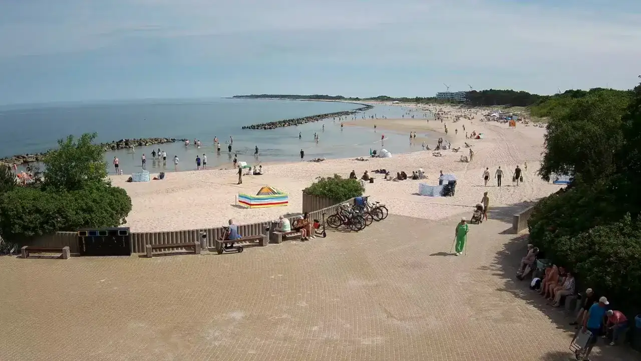 Słoneczny dzień w nadmorskim mieście nad Wieprzą. Ludzie spacerują po plaży, kąpią się w morzu i odpoczywają na piasku.