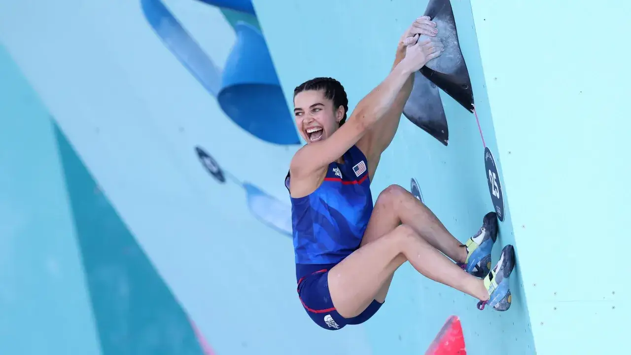 Brooke Raboutou, escaladora estadounidense, sonríe mientras se aferra a una pared de escalada azul.