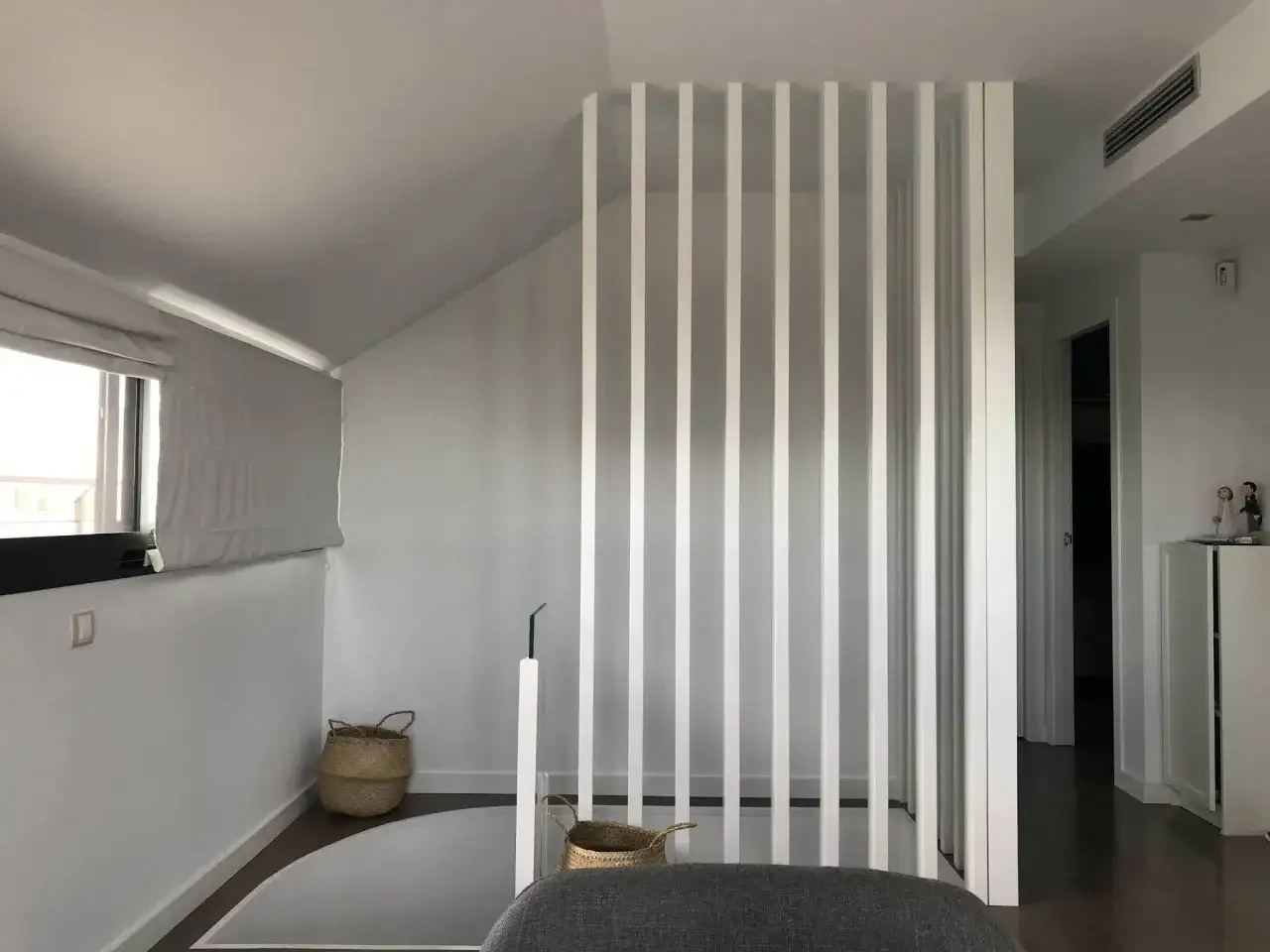 Modern interior with a white slatted partition, possibly to tirar tabique para unir dos pisos. Baskets and a window are visible.