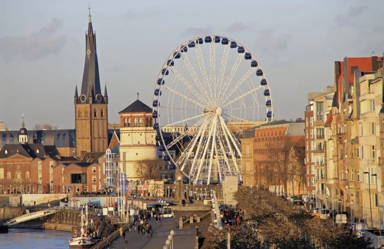 Rueda de la fortuna y arquitectura histórica en Düsseldorf. Un paseo fluvial con gente y barcos, ideal para saber qué ver en Düsseldorf.