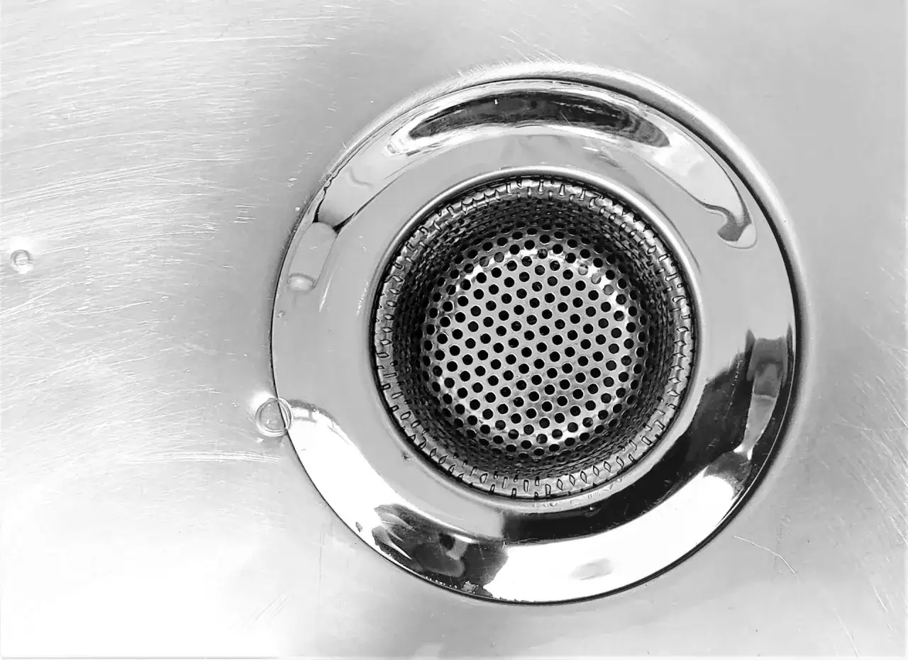 Primer plano de un desagüe de ducha metálico con rejilla perforada. Ideal para desatascar desagüe ducha y mantener el agua fluyendo.