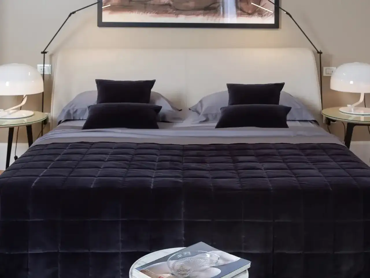 Un letto elegante con piumone scuro, cuscini coordinati e lampade moderne. Ecco come rifare il letto con piumone per un look impeccabile.