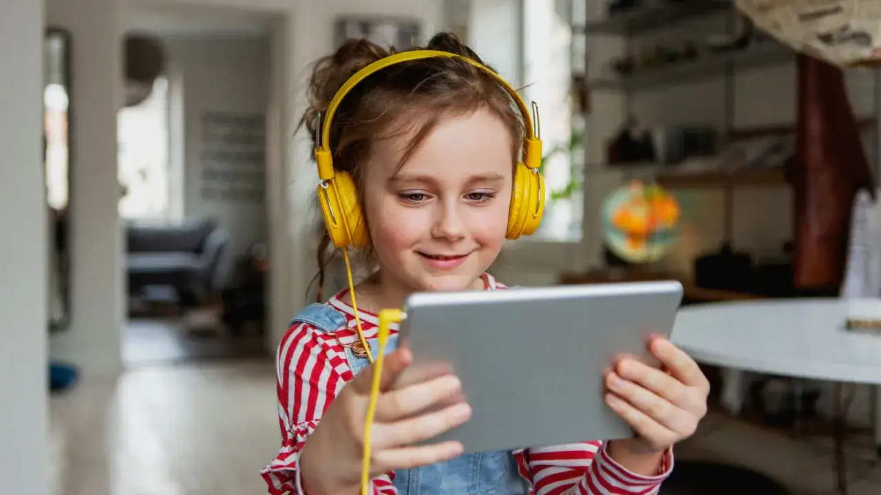 Niña con auriculares amarillos y tablet, aprendiendo y superando problemas de aprendizaje.