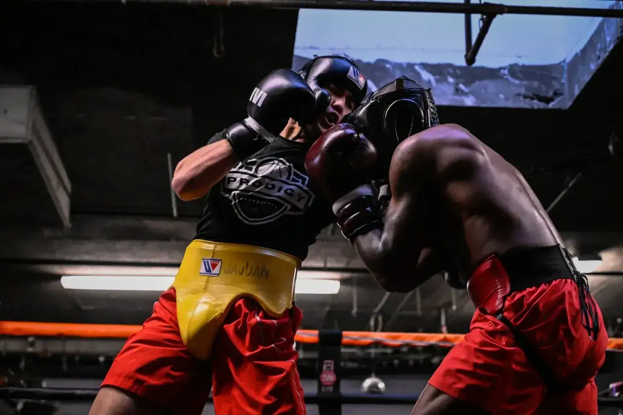 Two boxers in a sparring match, wearing headgear and gloves, intensely focused on the fight.
