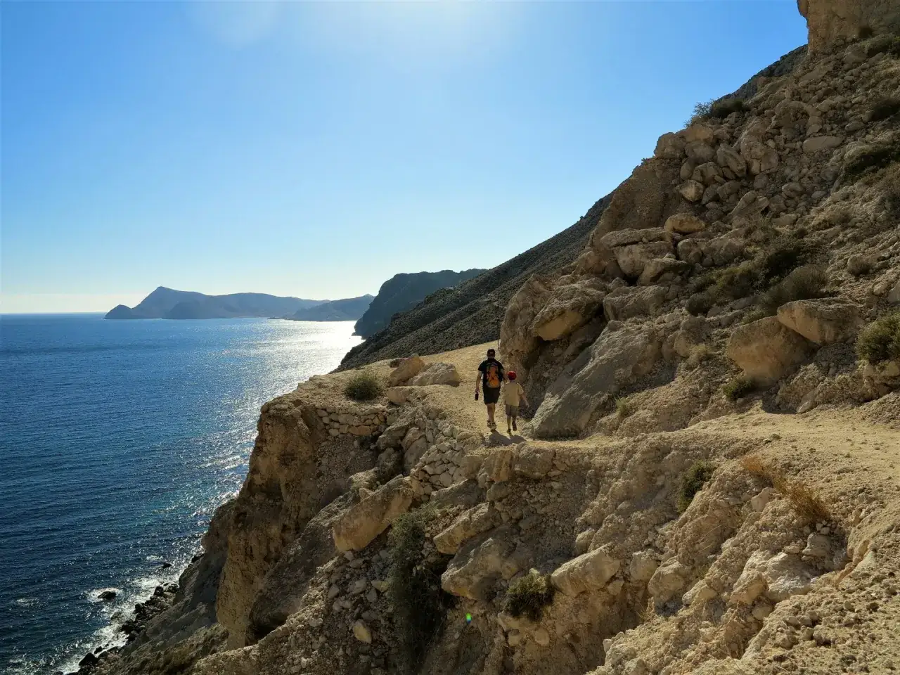 Dos personas disfrutan de una **randonnée en Cabo de Gata**, caminando por un sendero rocoso junto al mar azul.
