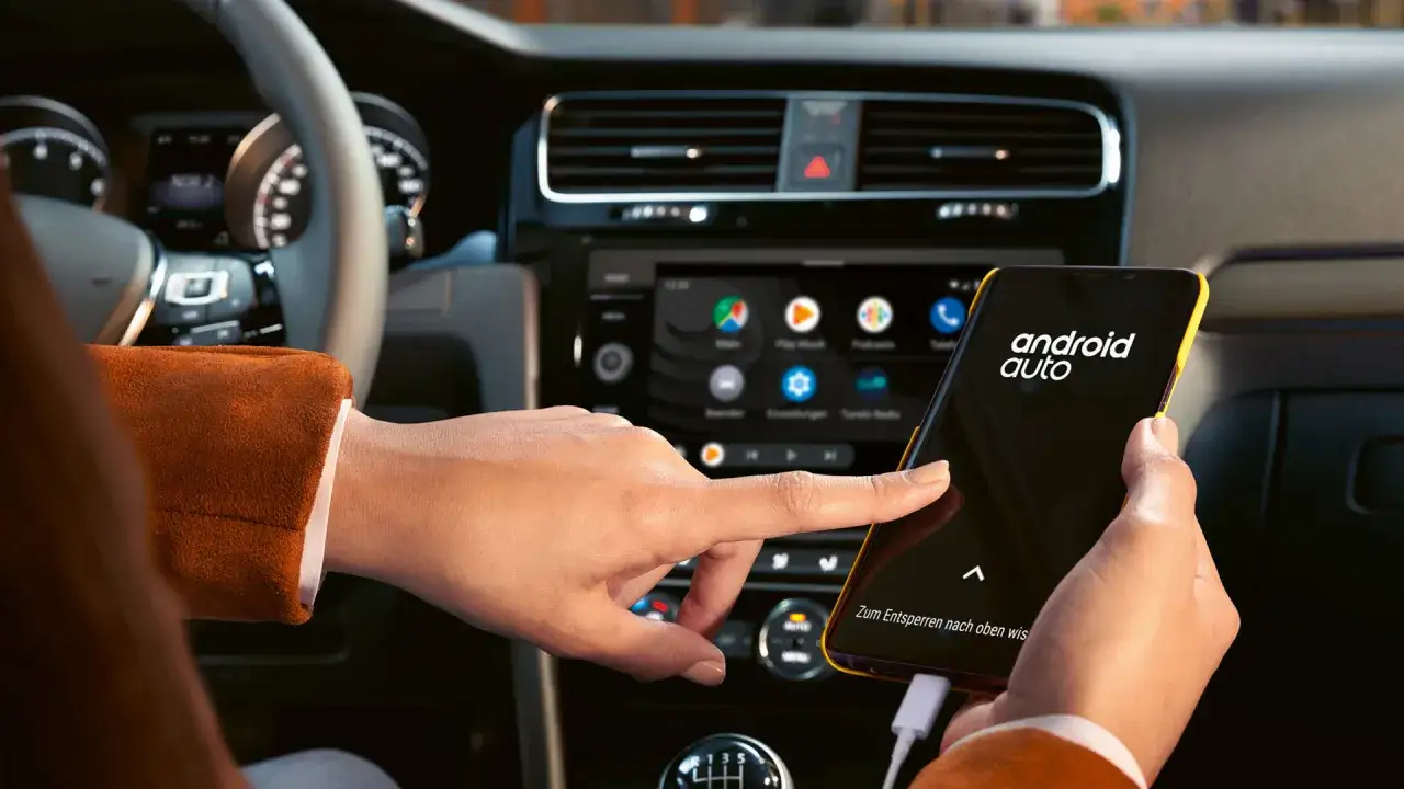 Une main interagit avec un smartphone affichant l'application android auto, connect&eacute; &agrave; l'&eacute;cran du tableau de bord d'une voiture.