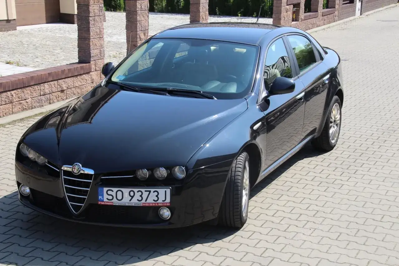 Czarny Alfa Romeo 159 1.9 JTD z tablicą rejestracyjną SO 9373J stoi na kostce brukowej.