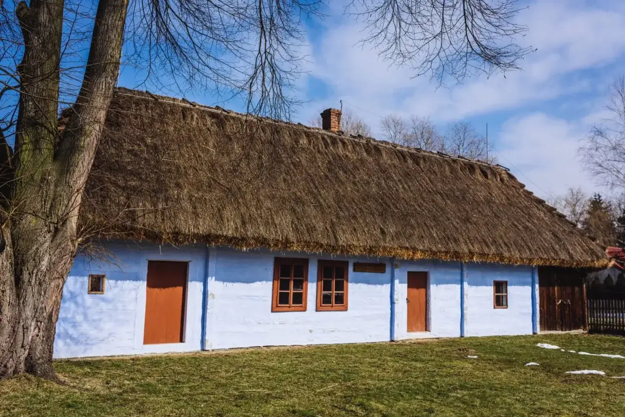 Tradycyjny dom z niebieskimi ścianami i strzechą. Ciekawostki o Wincentym Witosie mogą być związane z takimi miejscami.