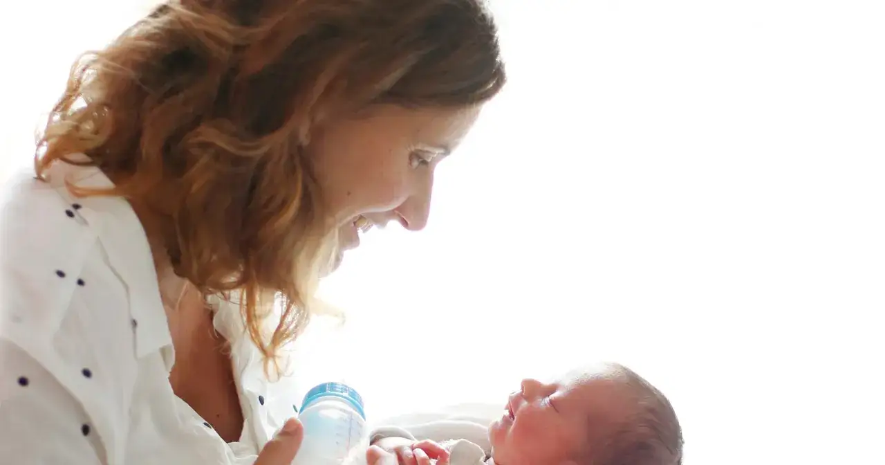 Uśmiechnięta mama karmi butelką noworodka. To piękny okres, choć karmienie piersią bywa wyzwaniem.