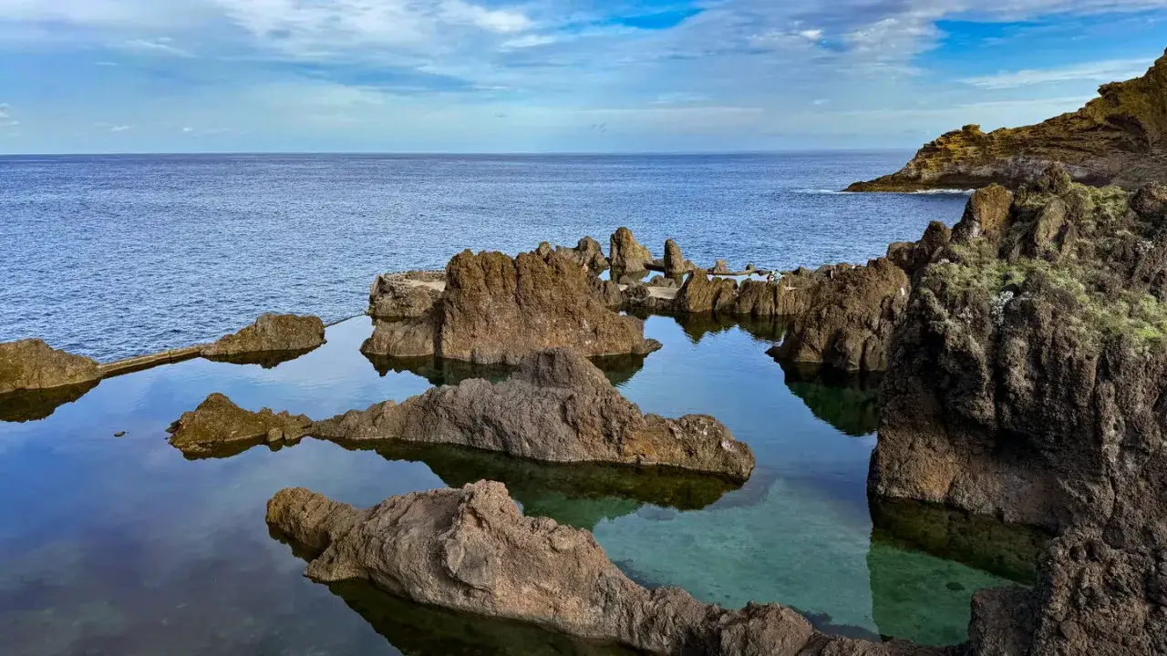 Naturschwimmbecken auf Madeira, umgeben von vulkanischem Gestein, mit klarem Wasser und dem weiten Ozean im Hintergrund.
