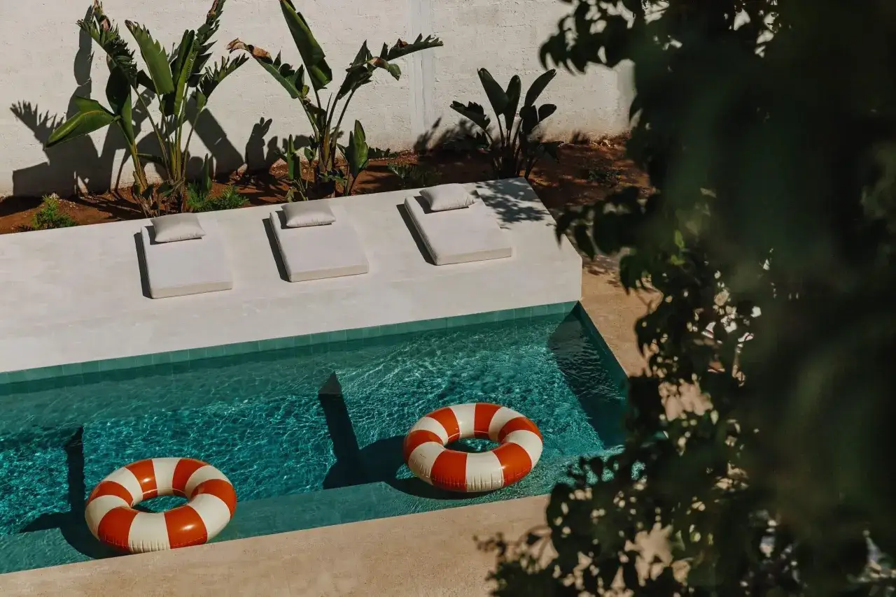 Piscine d'un gîte en Italie, avec des bouées rayées orange et blanches, des transats et des plantes luxuriantes.