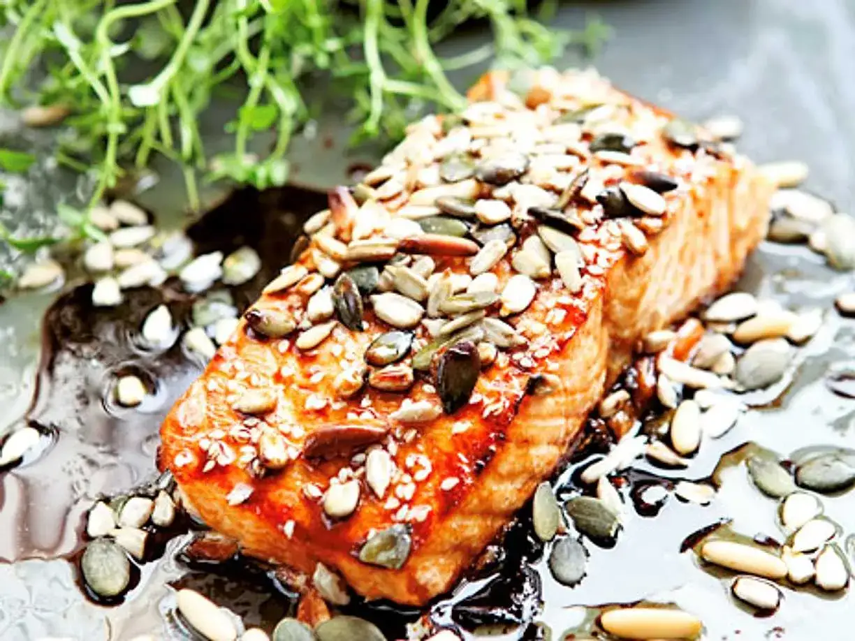 En saftig bit asiatisk lax i ugn, toppad med en blandning av frön och sesam. Serverad i en glansig sås med gröna örter.