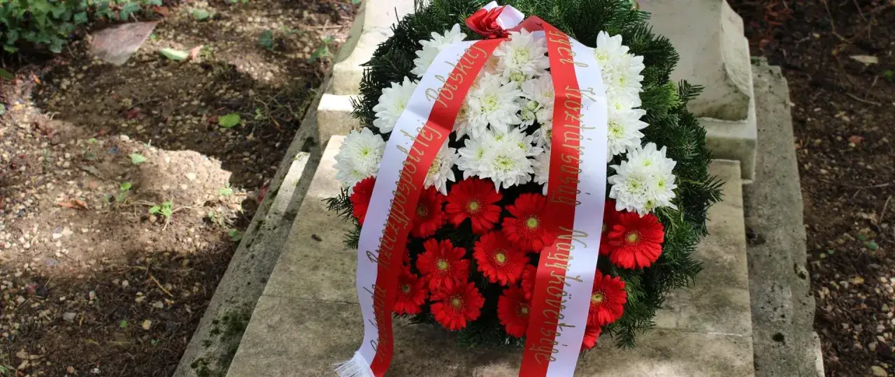 Wieniec z białych i czerwonych kwiatów na grobie. Wstęga z napisem
