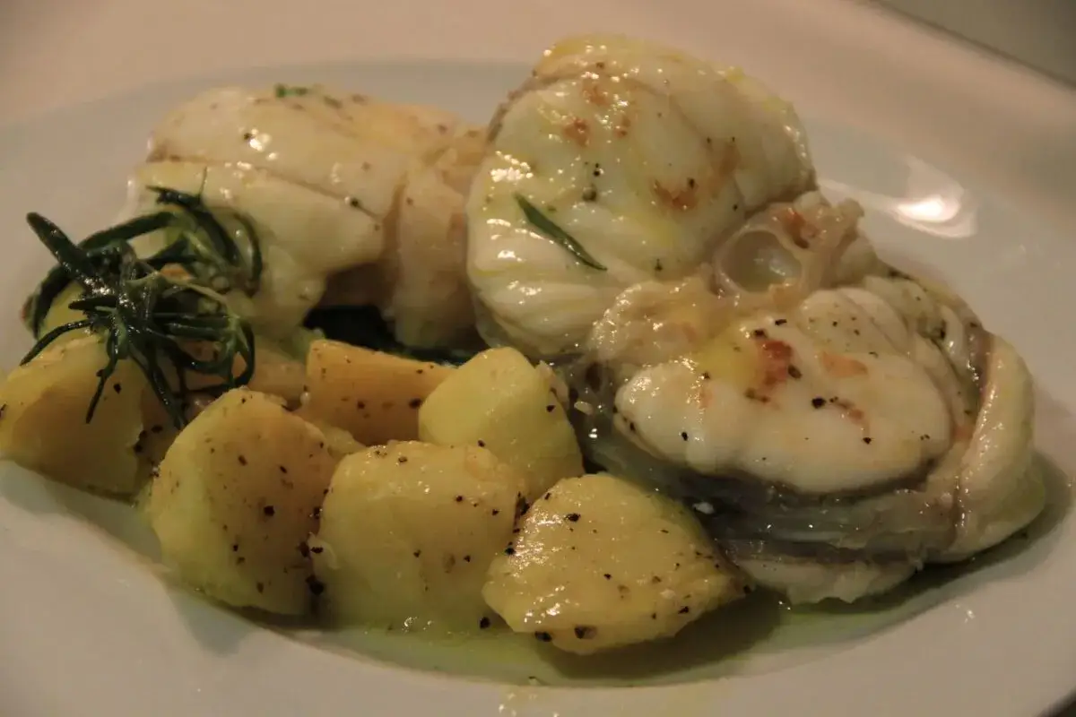 Rape a la plancha con patatas y romero. El pescado blanco, tierno y jugoso, reposa sobre patatas doradas y hierbas aromáticas.