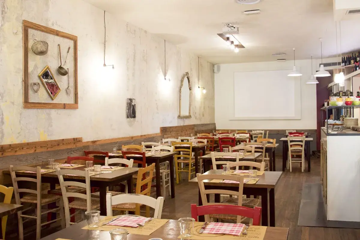 Interno di un ristorante accogliente, con tavoli apparecchiati e sedie colorate. Sembra il posto perfetto per una cena da