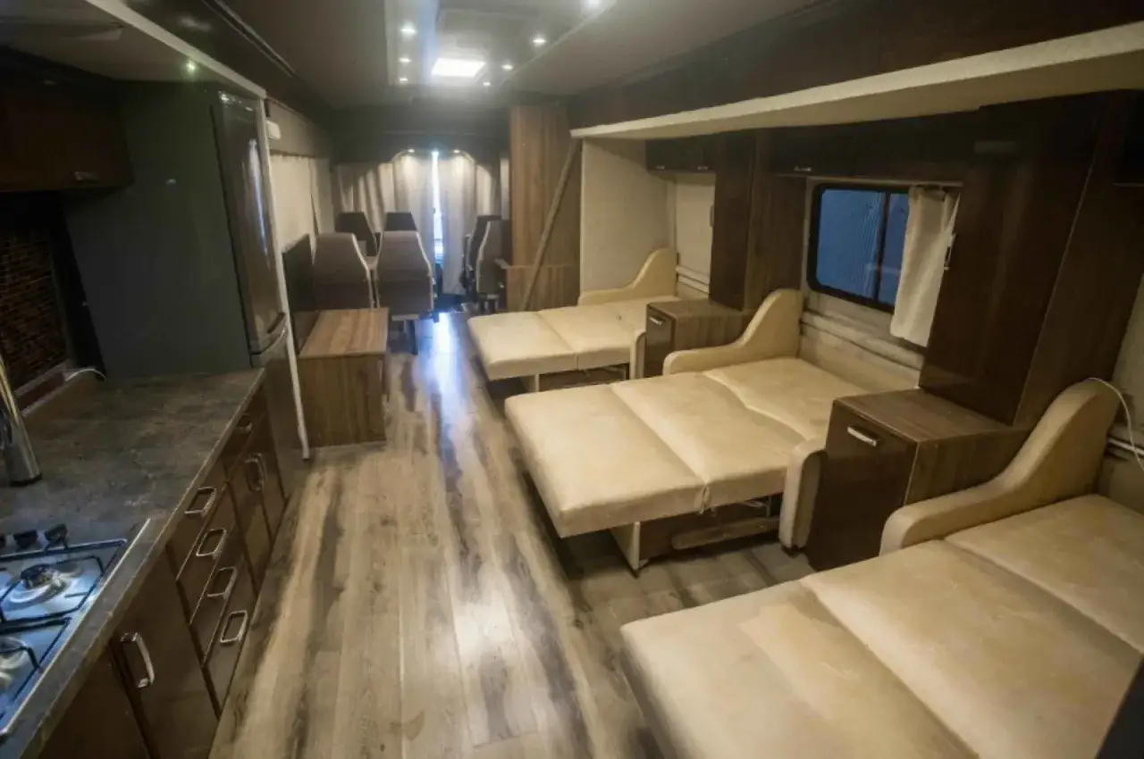 Wnętrze autobusu kempingowego z rozkładanymi łóżkami, aneksem kuchennym i miejscami do siedzenia.