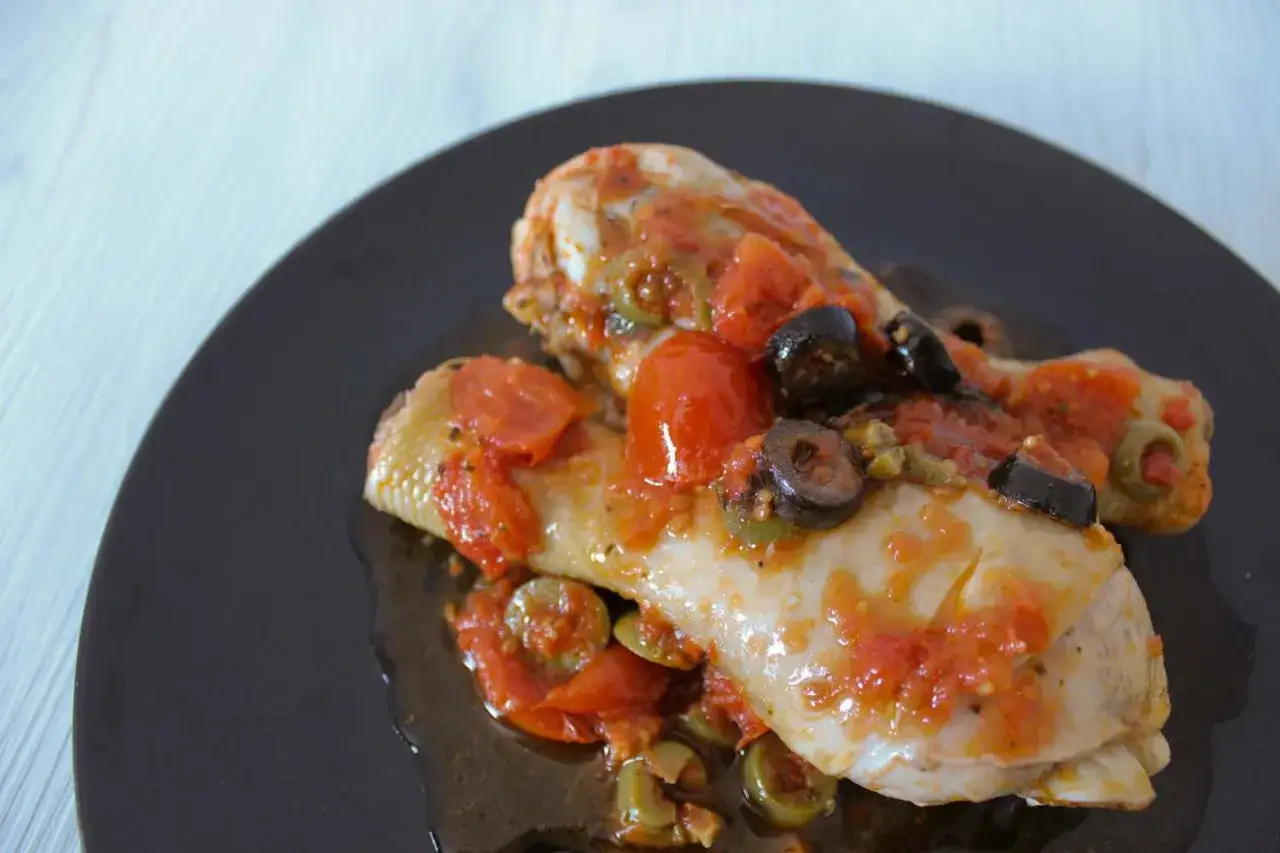Cosce di pollo in padella, succulente e saporite, condite con pomodoro e olive nere.