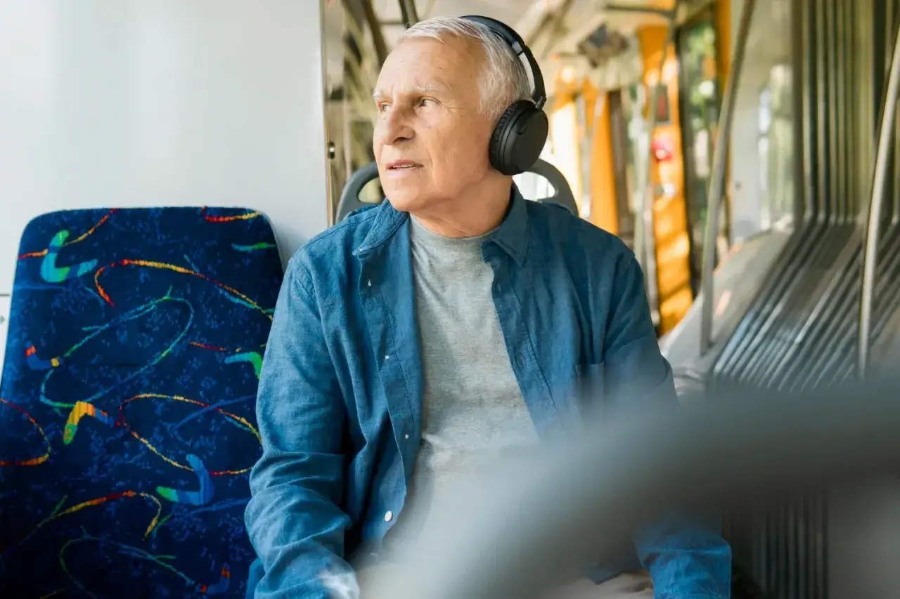 Kto to jest senior? To mężczyzna w słuchawkach, który podróżuje autobusem, słuchając muzyki.