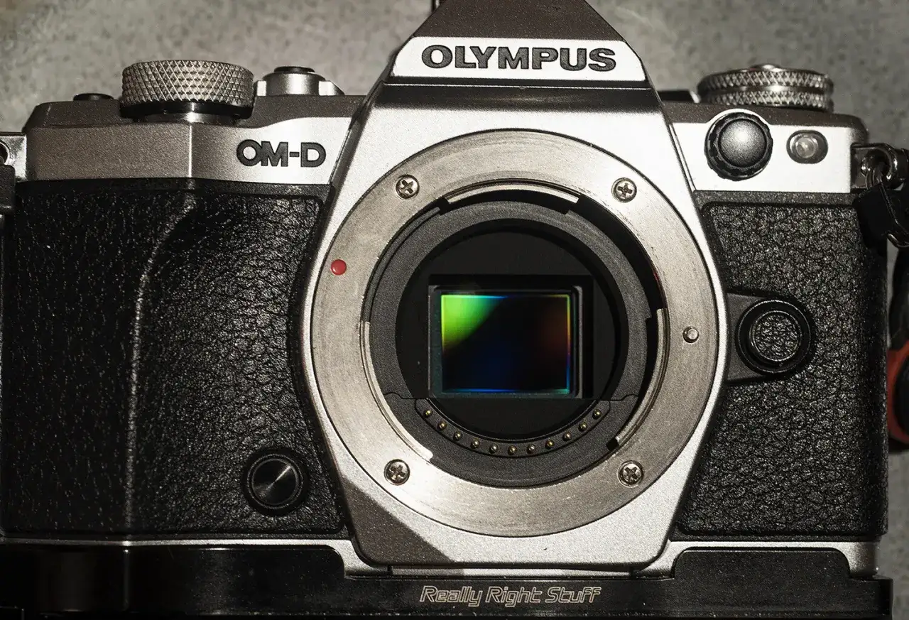 Srebrny aparat Olympus OM-D z widocznym sensorem, kt&oacute;ry dzięki technologii pixel shift pozwala na uchwycenie niezwykłych detali.