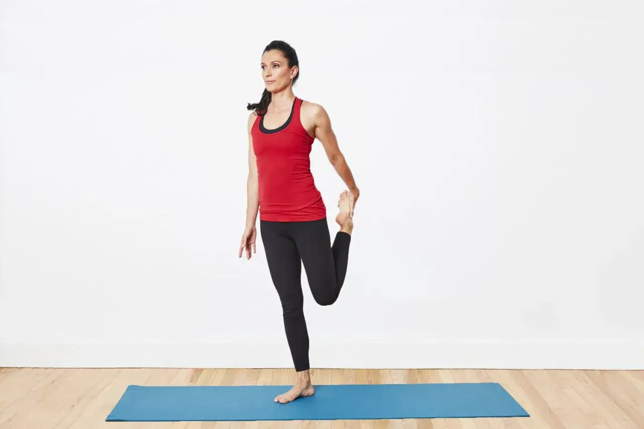 Femme en tenue de sport effectuant un &eacute;tirement quadriceps sur un tapis bleu.