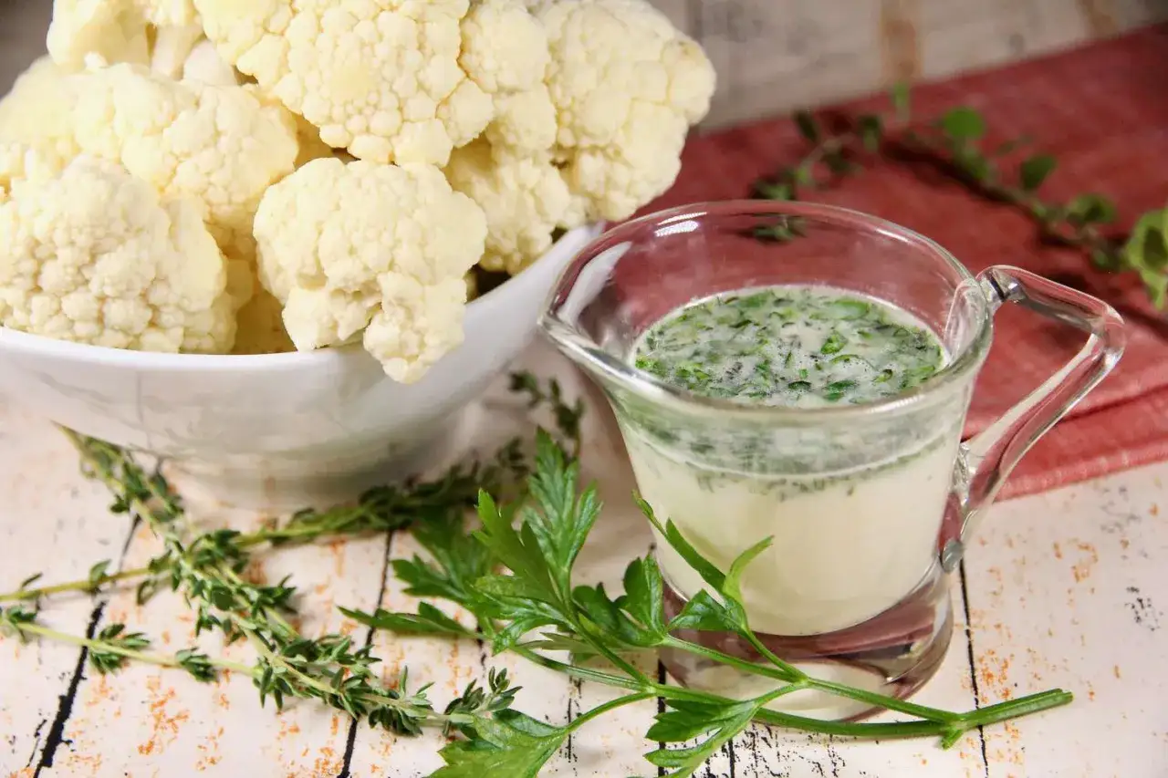 En skål med blomkål och en liten karaff med en krämig sås med örter. Perfekt för ett café de Paris sås recept.