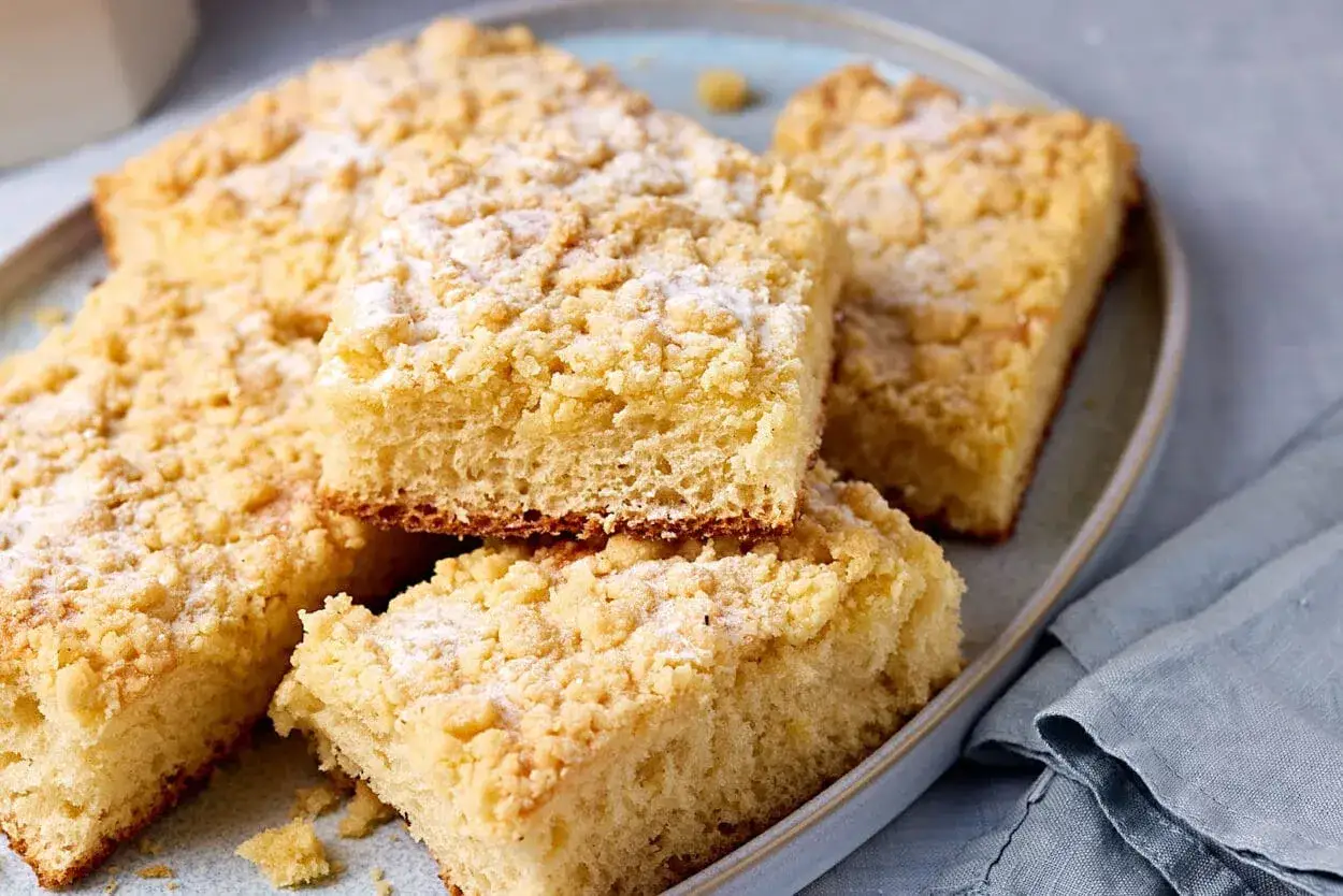 Saftiger Streuselkuchen vom Blech, mit Puderzucker bestäubt, auf einem Teller angerichtet.