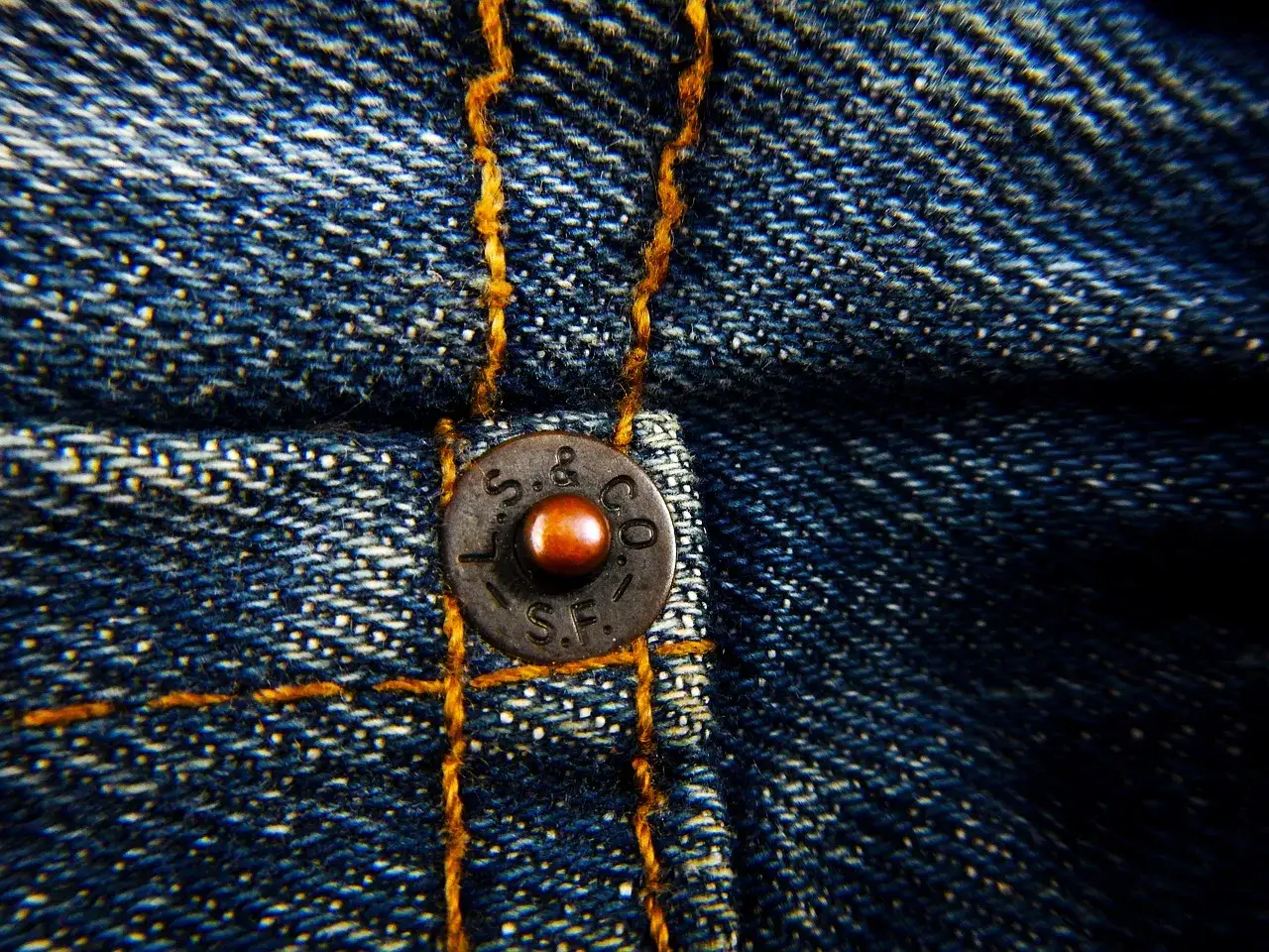 Close-up of a vintage jeans bouton, showing the textured denim and copper rivet.