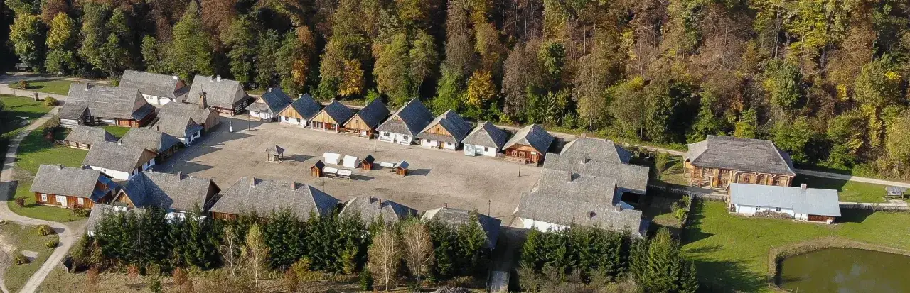 Widok z lotu ptaka na największy skansen w Polsce, z drewnianymi chatami i budynkami gospodarczymi otaczającymi dziedziniec.